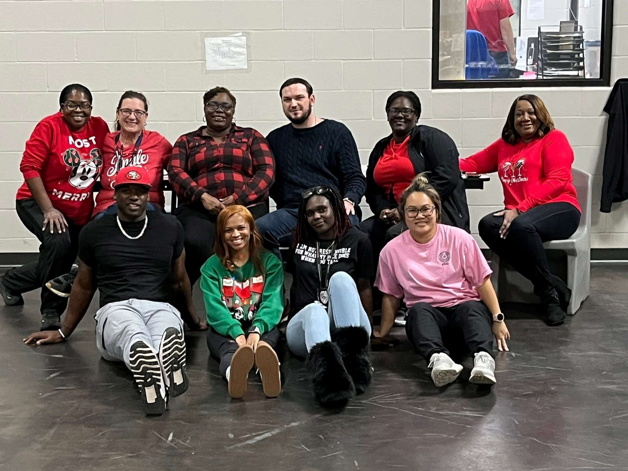 Group of ten staff members posing indoors in a common area, several wearing red and green holiday-themed clothing.