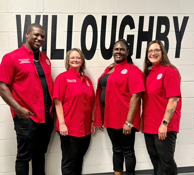 Group of four staff members posing indoors in a common area, wearing red shirts.